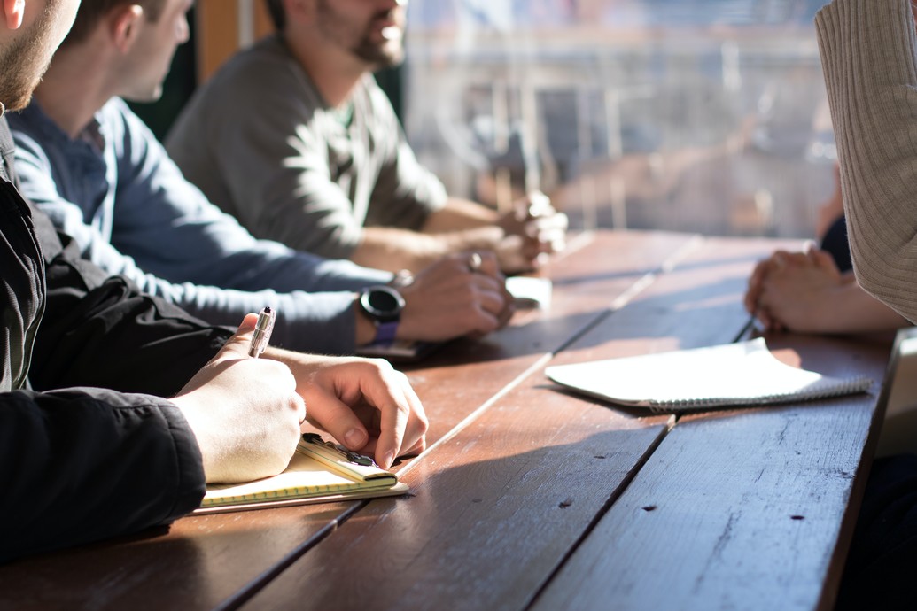 A group of people sat around a wooden table, taking notes