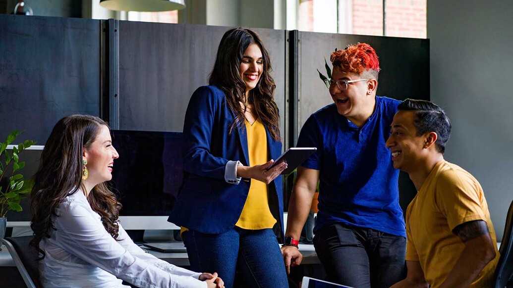 A group of people smiling at each other while one holds a tablet